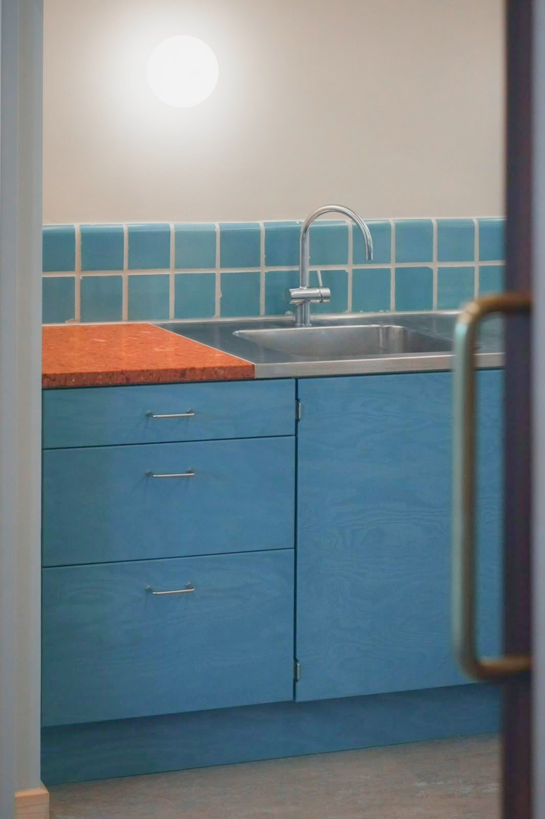 Kitchenette with blue plywood fronts and a stainless steel worktop at Mørkhøj School