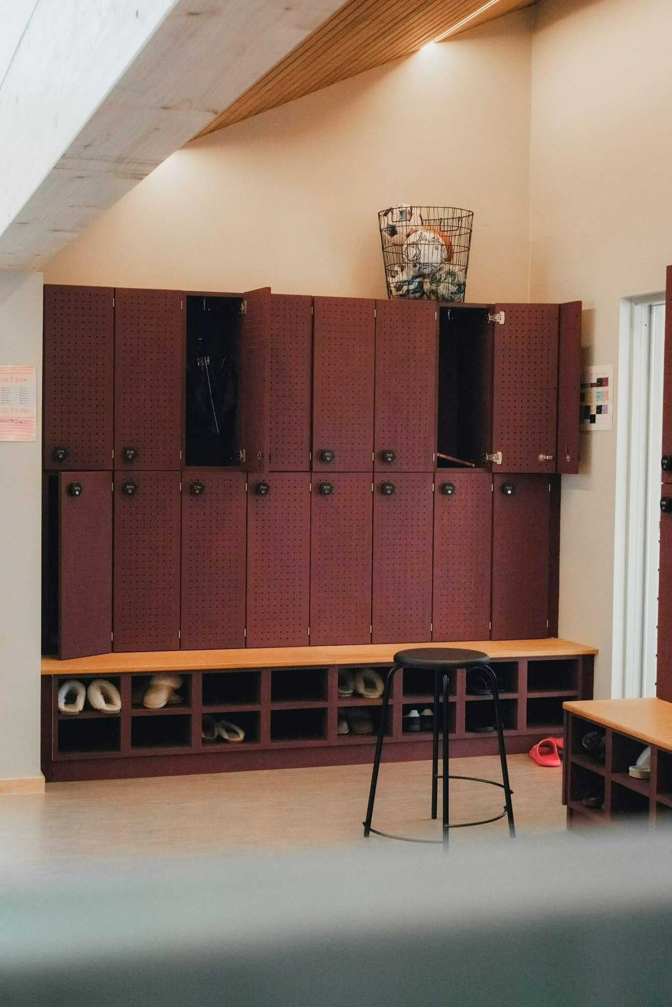 Røde lockers med perforerede låger og kodelås over en bænk med skohylder